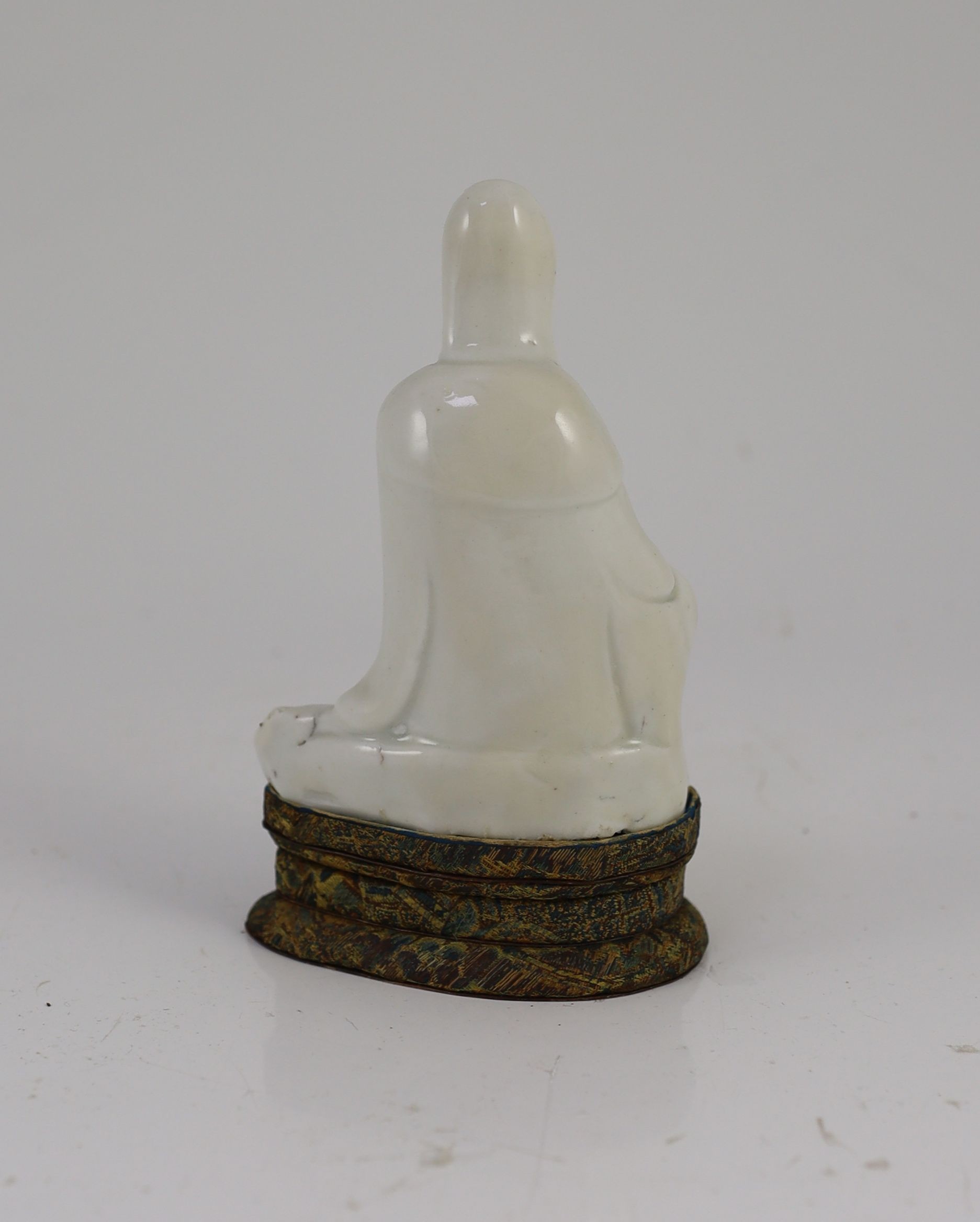 A Chinese blanc-de-chine seated figure of Guanyin, Dehua kilns, 18th century, 12cm high, Brocade covered stand